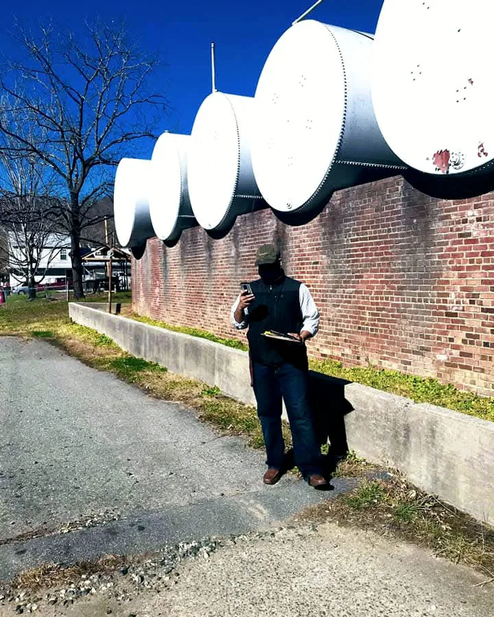Representative recording tank details on a phone and clipboard beside a row of storage tanks